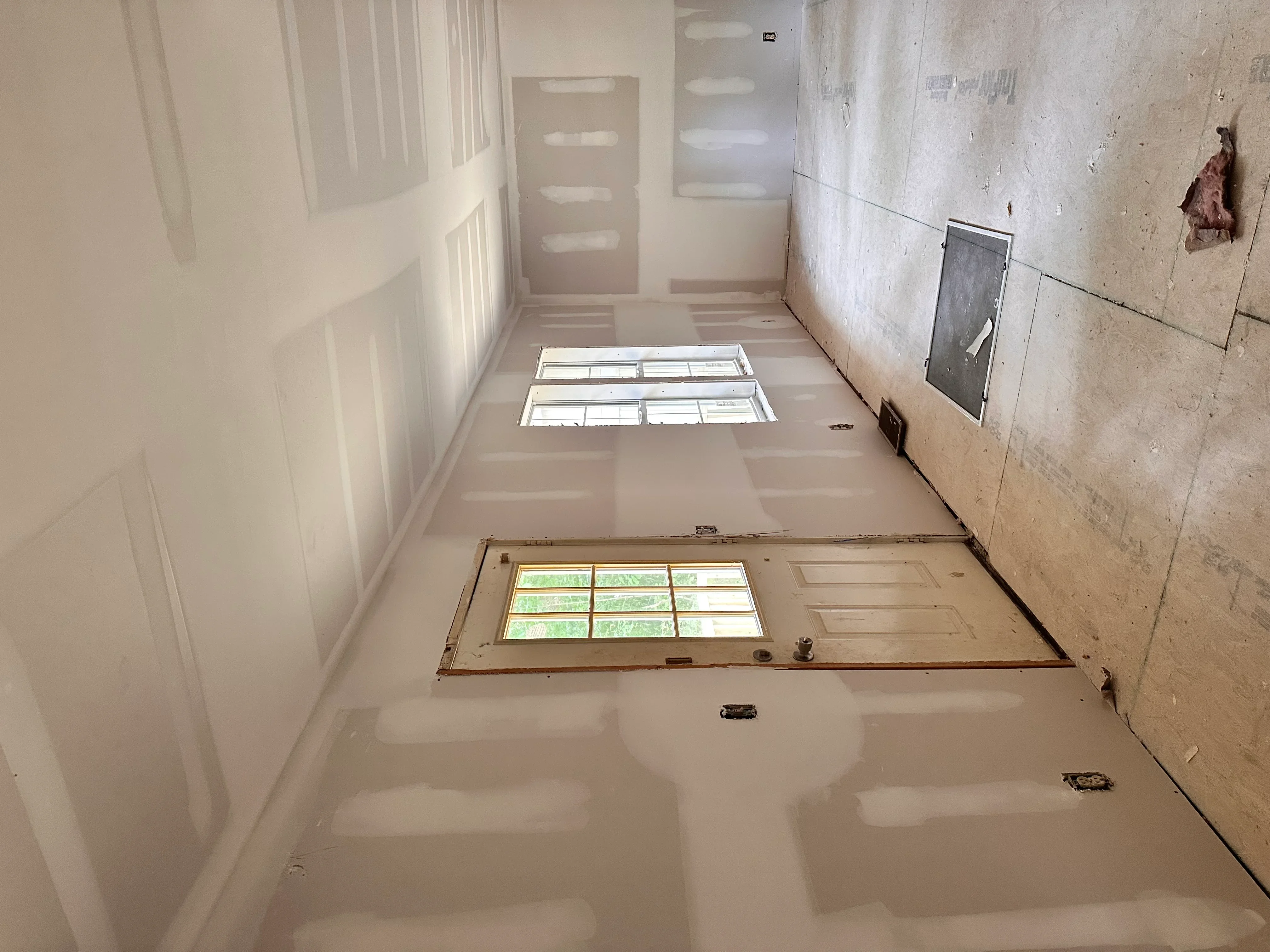 Hallway with finished drywall, taped seams, recessed lighting, and prepared surfaces ready for paint