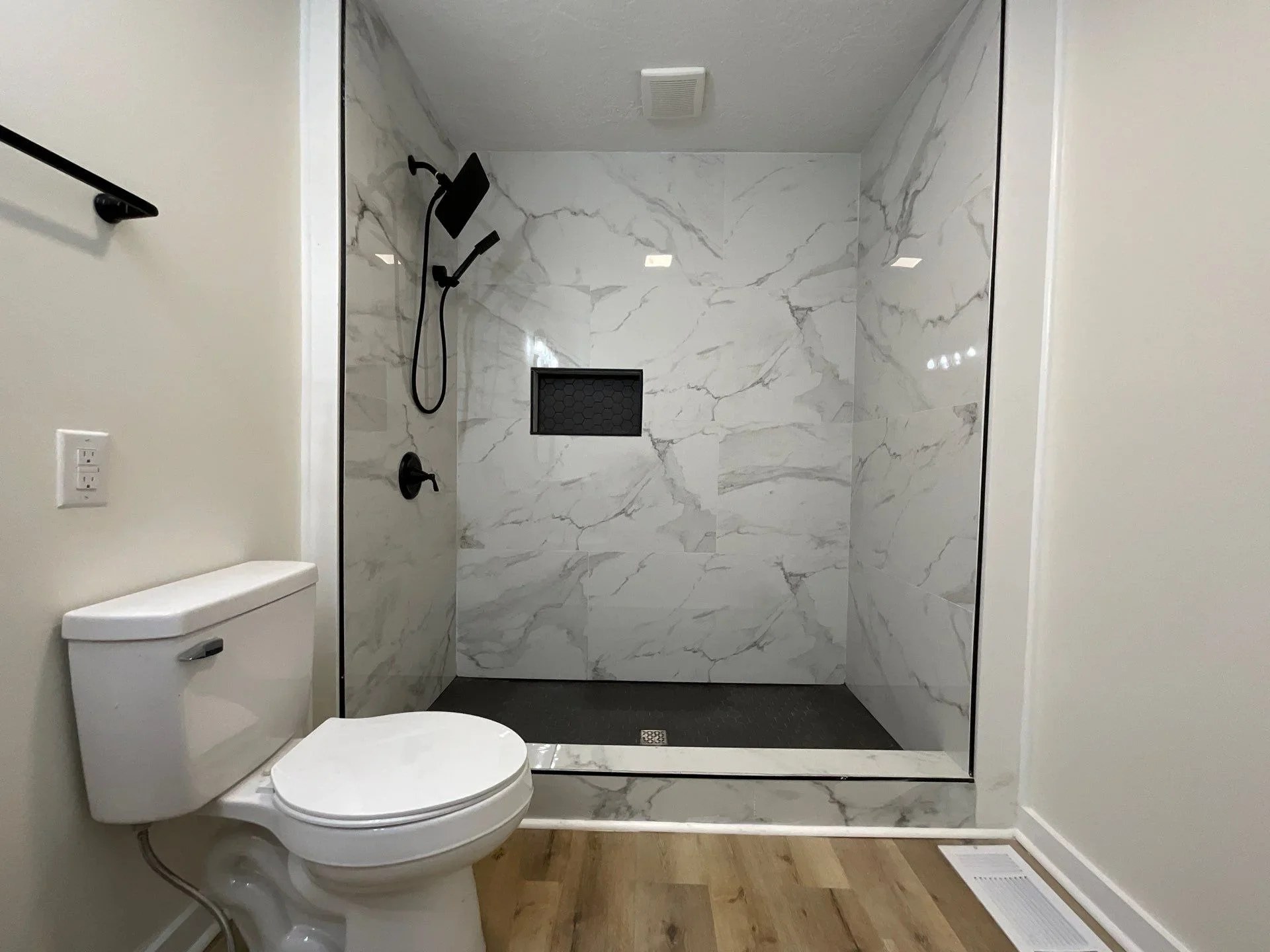 Modern bathroom with marble tile shower, black fixtures, and frameless glass enclosure