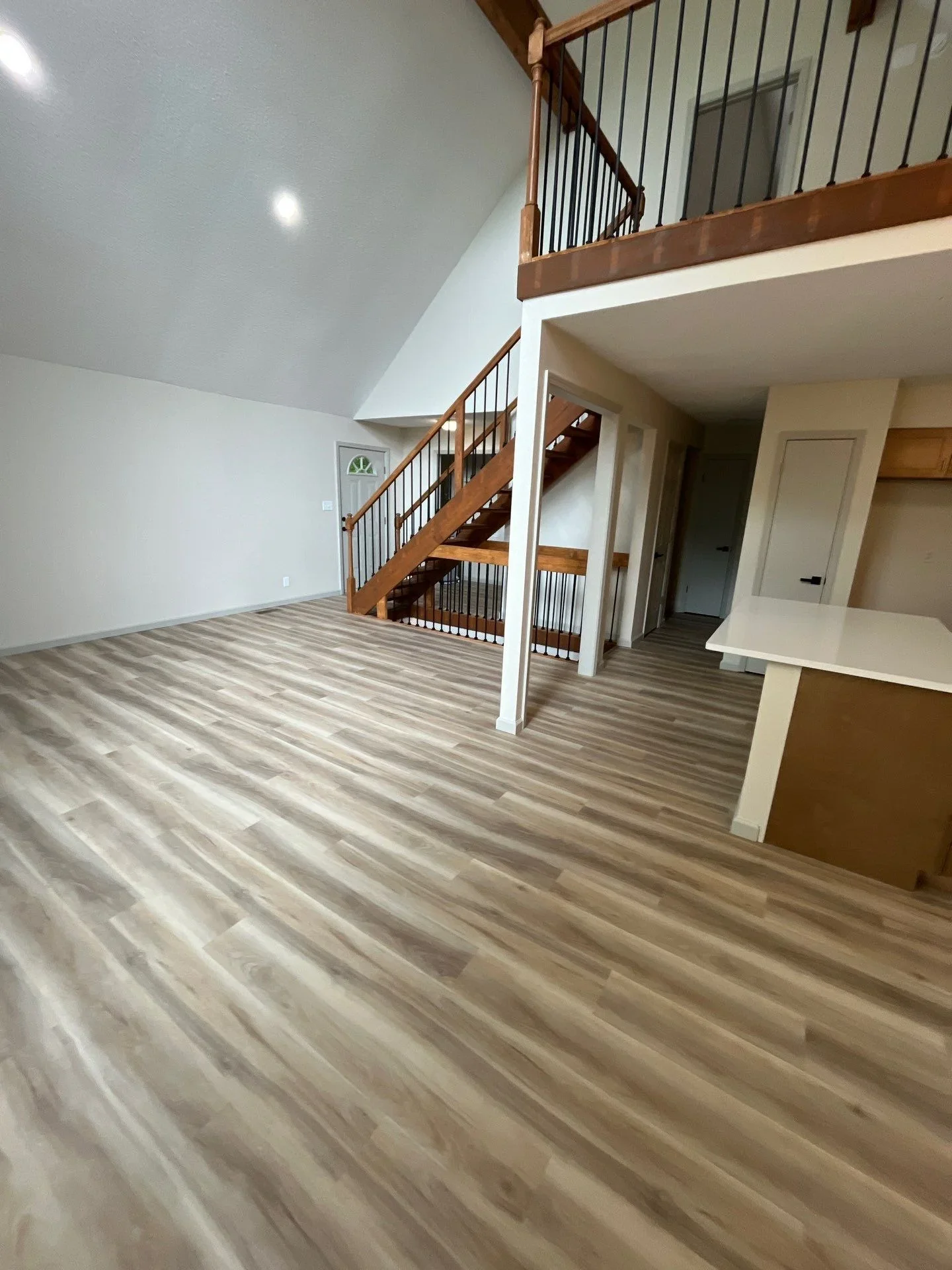 Open loft with luxury vinyl plank flooring, wood staircase with metal railings, and white drywall finishes