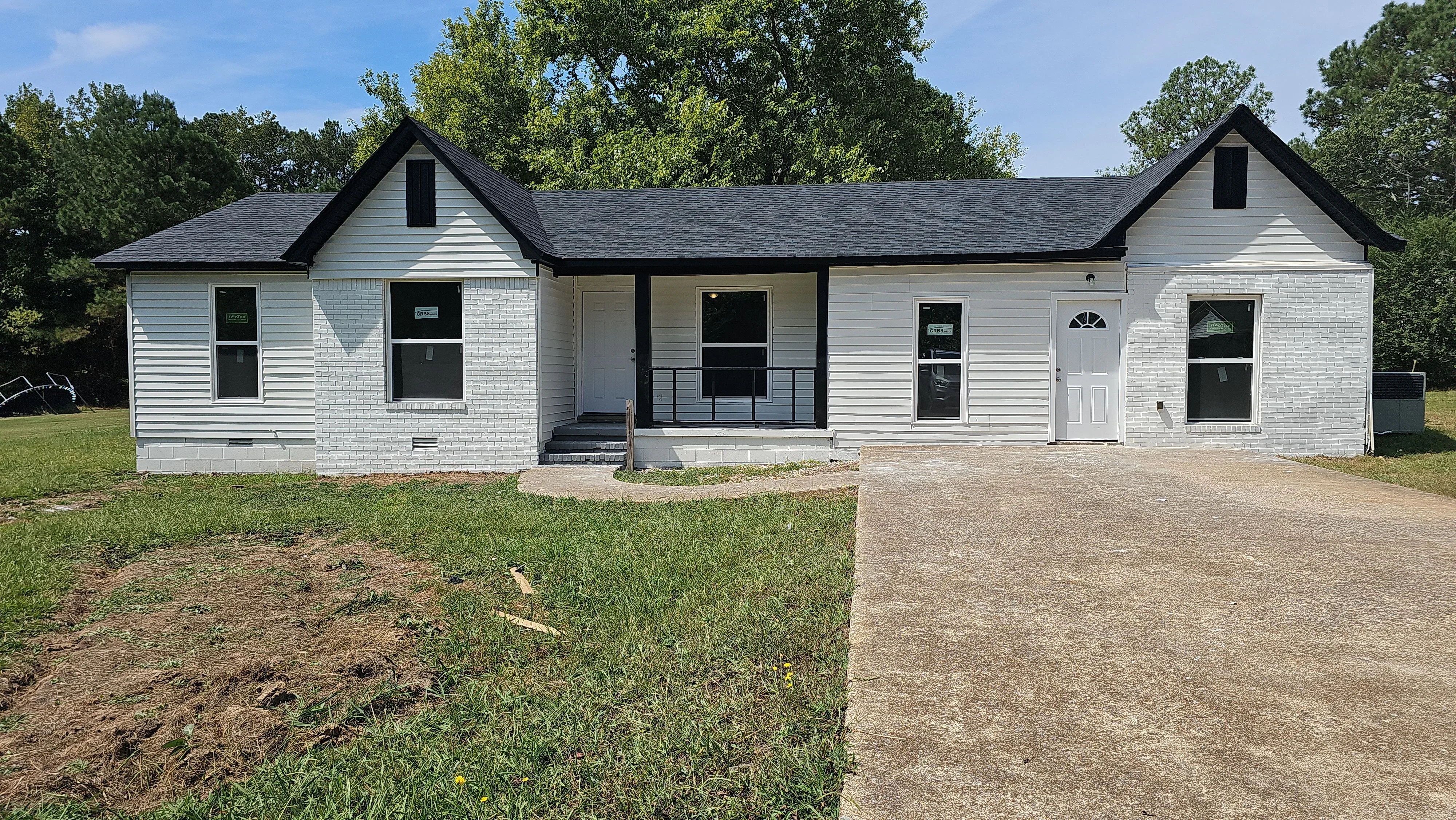 White vinyl siding home with black roof, covered porch, metal railings, and concrete driveway