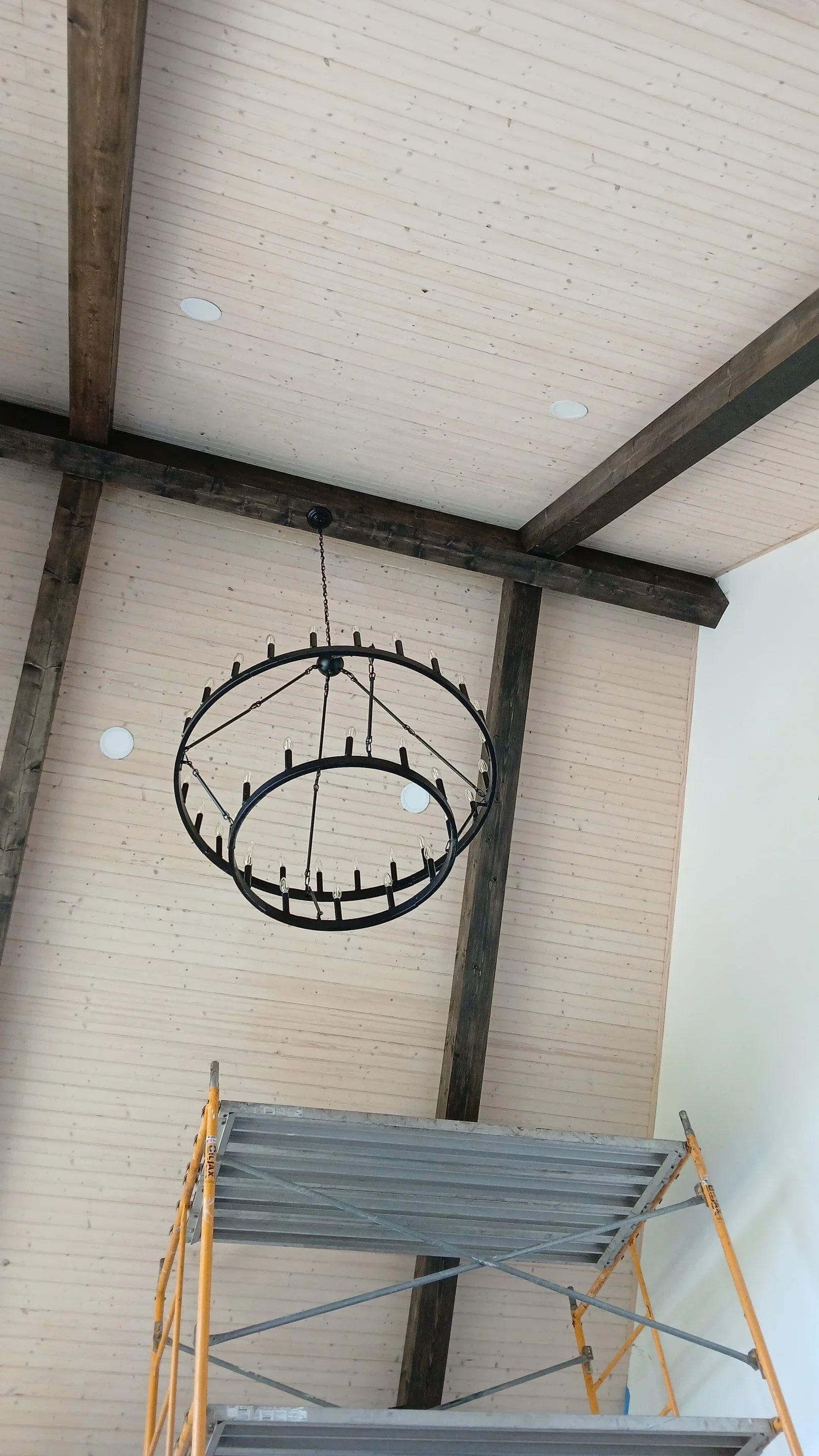 Whitewashed shiplap ceiling with exposed timber beams, recessed lights, and black iron chandelier