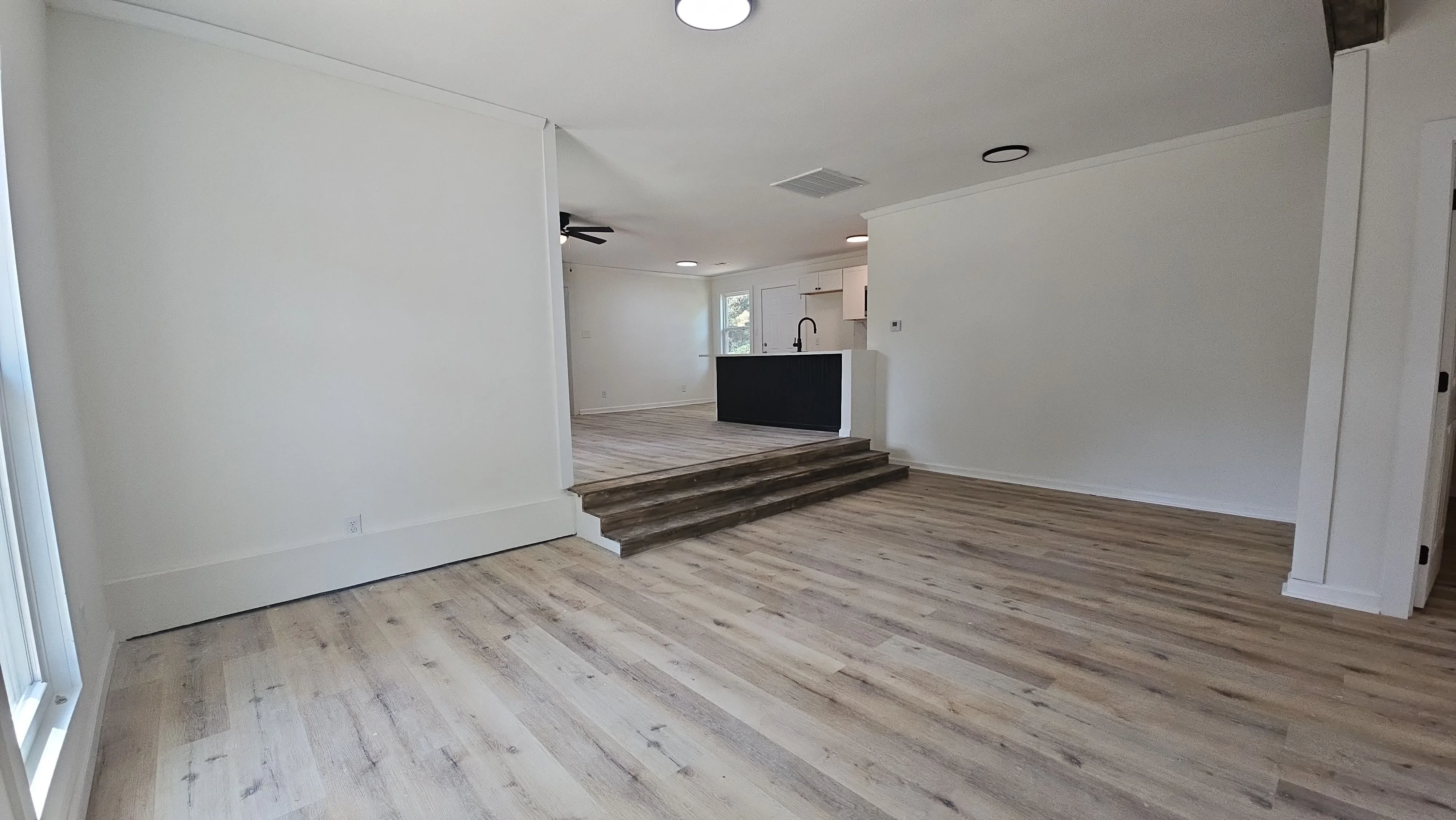 Open concept space with luxury vinyl plank flooring, white drywall, black kitchen island, and recessed lighting