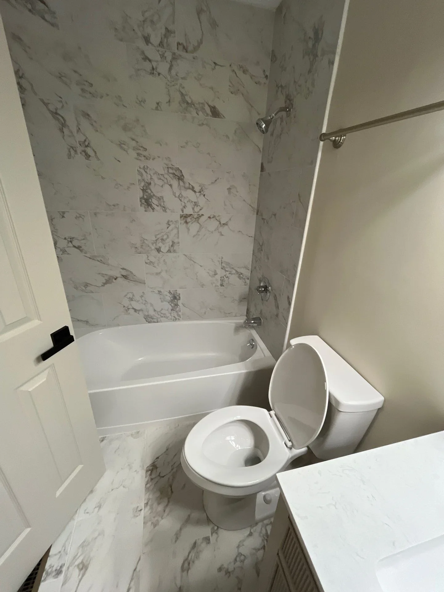 Marble tile bathroom with white bathtub, toilet, and chrome fixtures