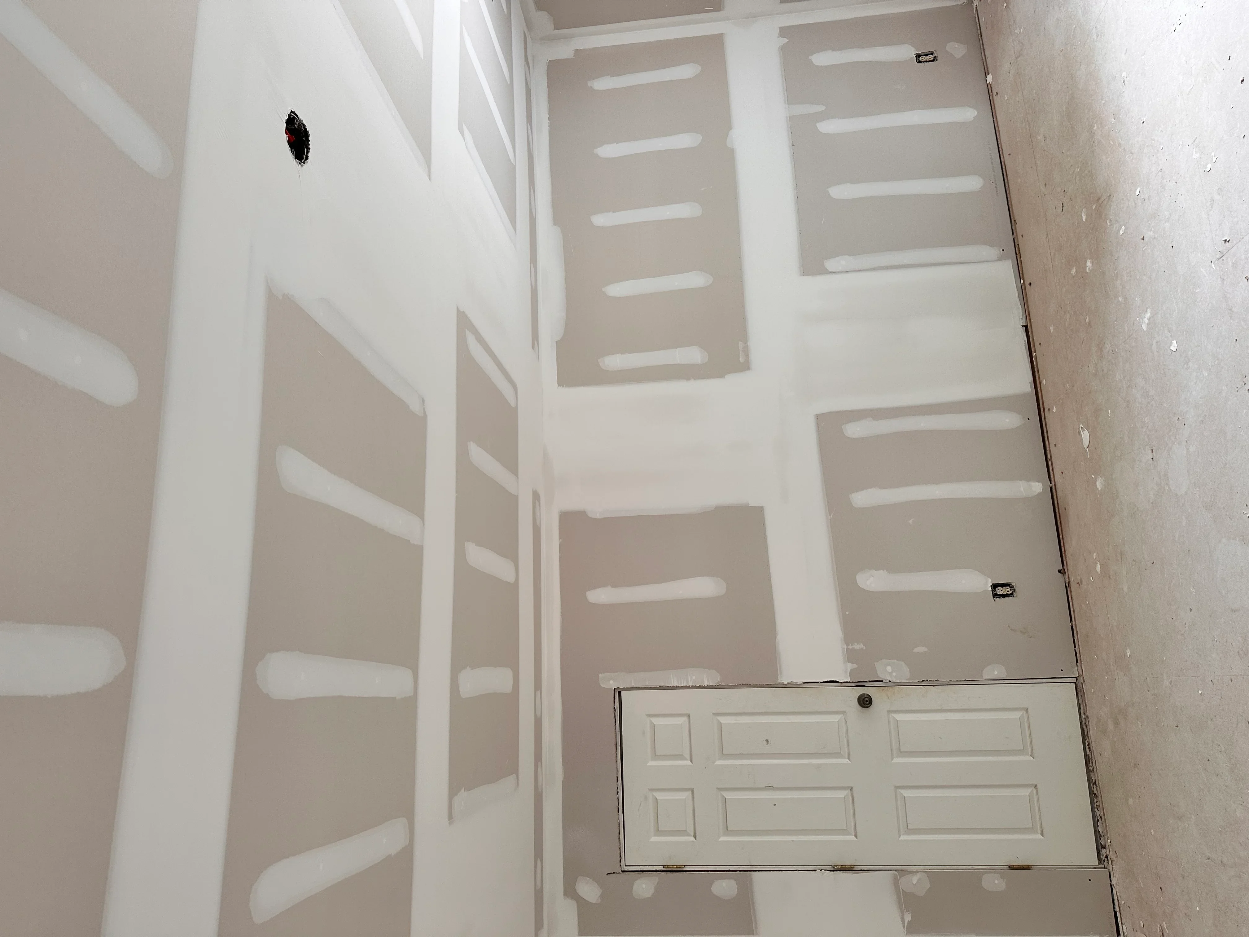 Drywall installation with taped joints, white trim framing, and recessed light openings in interior renovation
