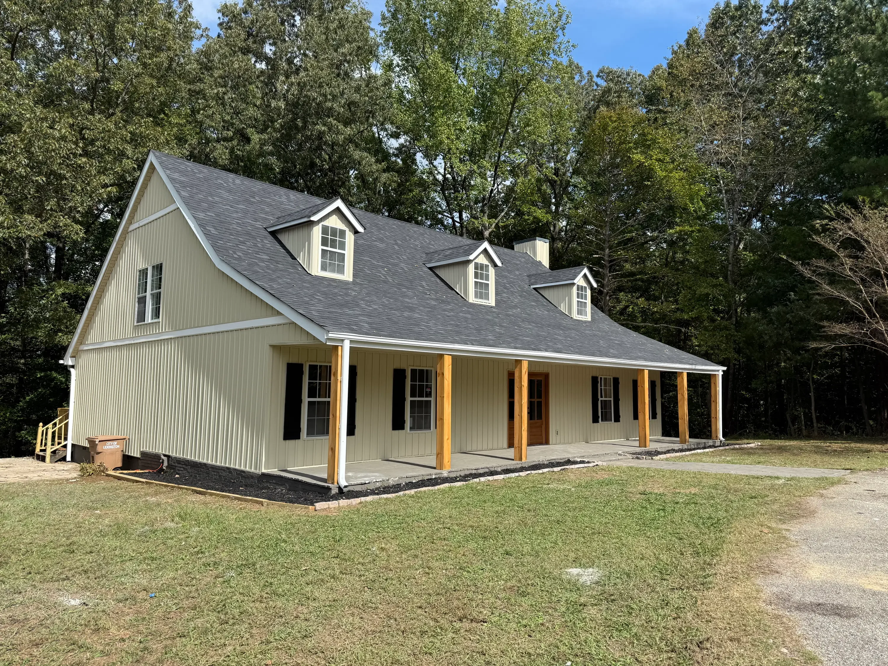 New farmhouse with cream siding, gray metal roof, three dormers, and front porch with wooden posts