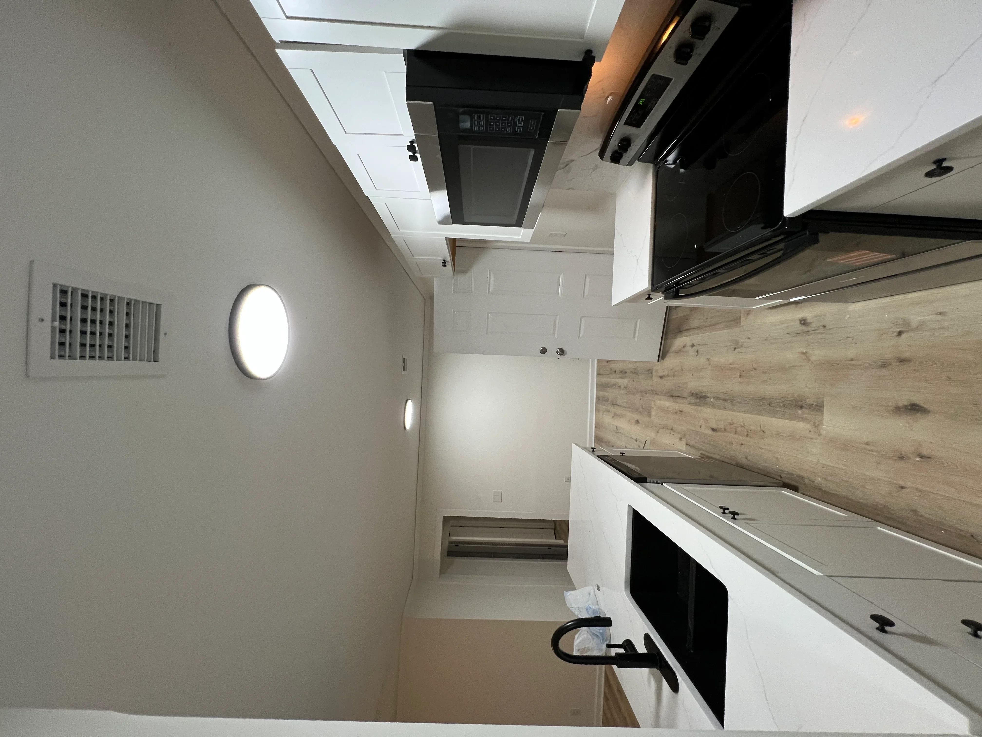 Modern kitchen with white cabinets, stainless steel appliances, wood backsplash, and recessed lighting