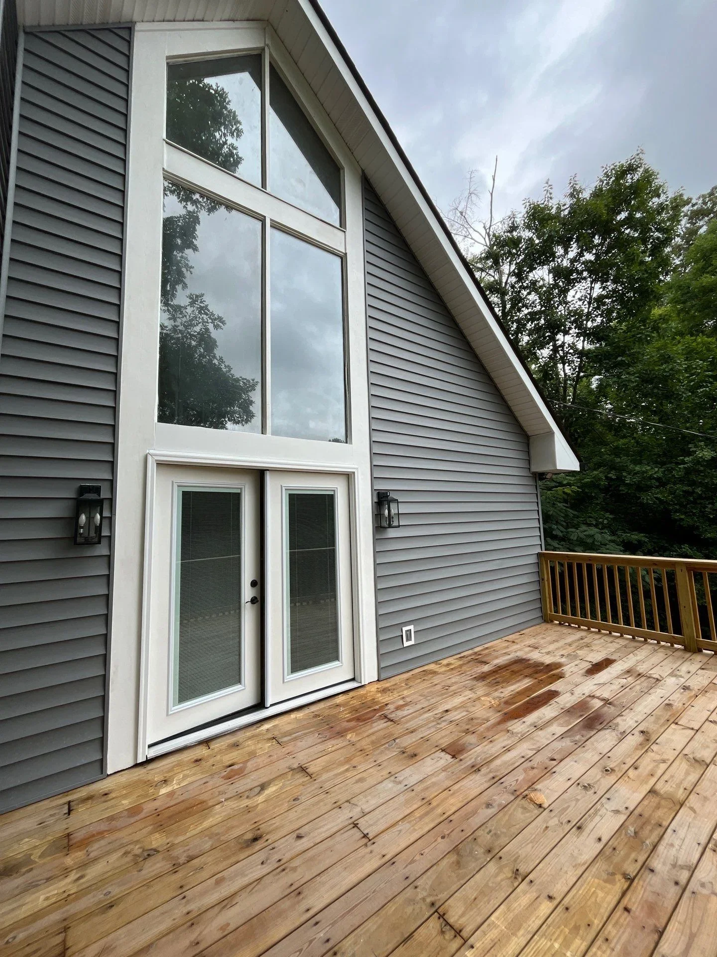 New wood deck with white-framed glass doors and large windows on gray siding exterior