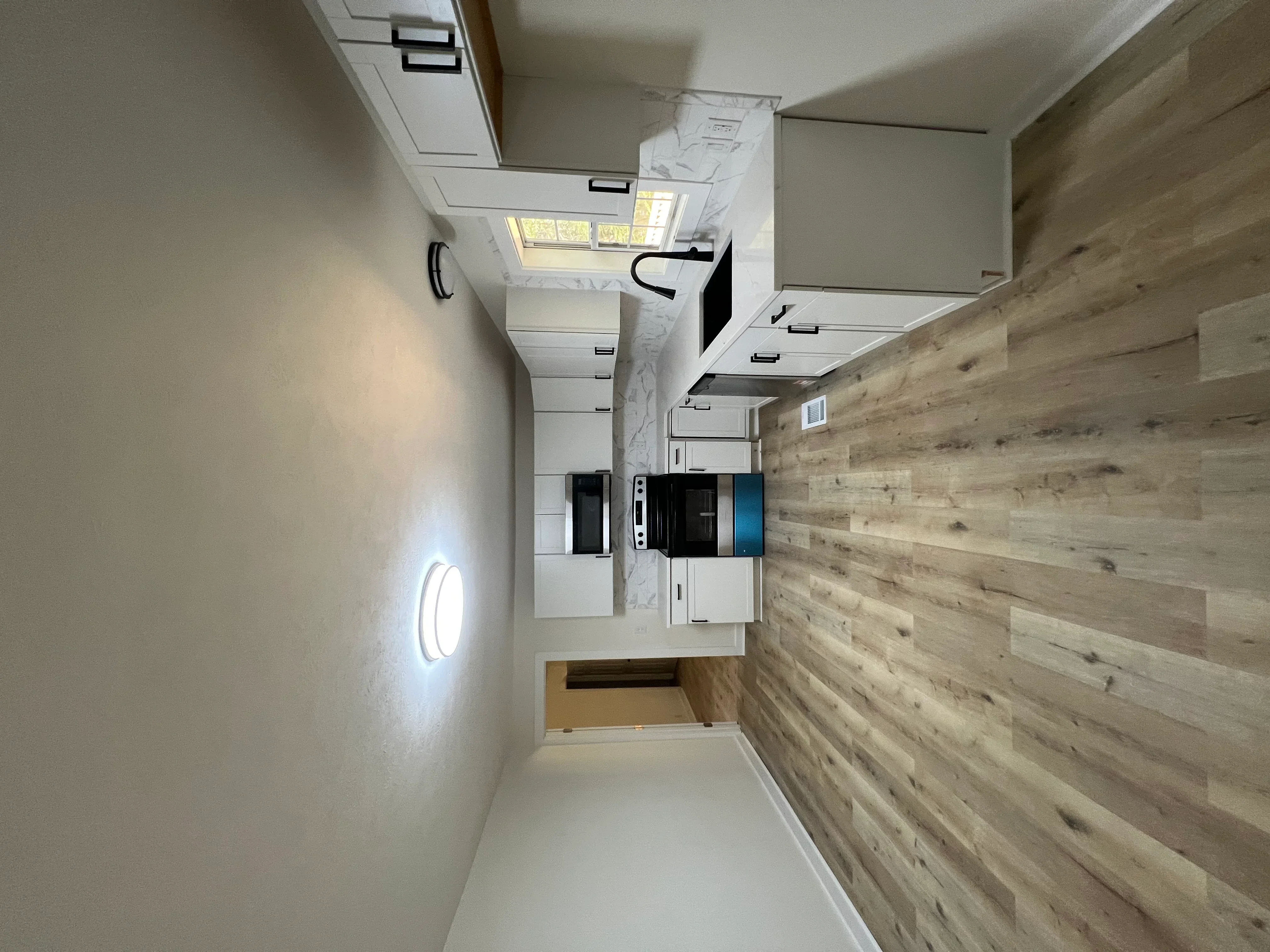 Modern kitchen with white cabinetry, marble counters, wood-grain vinyl flooring, and skylight